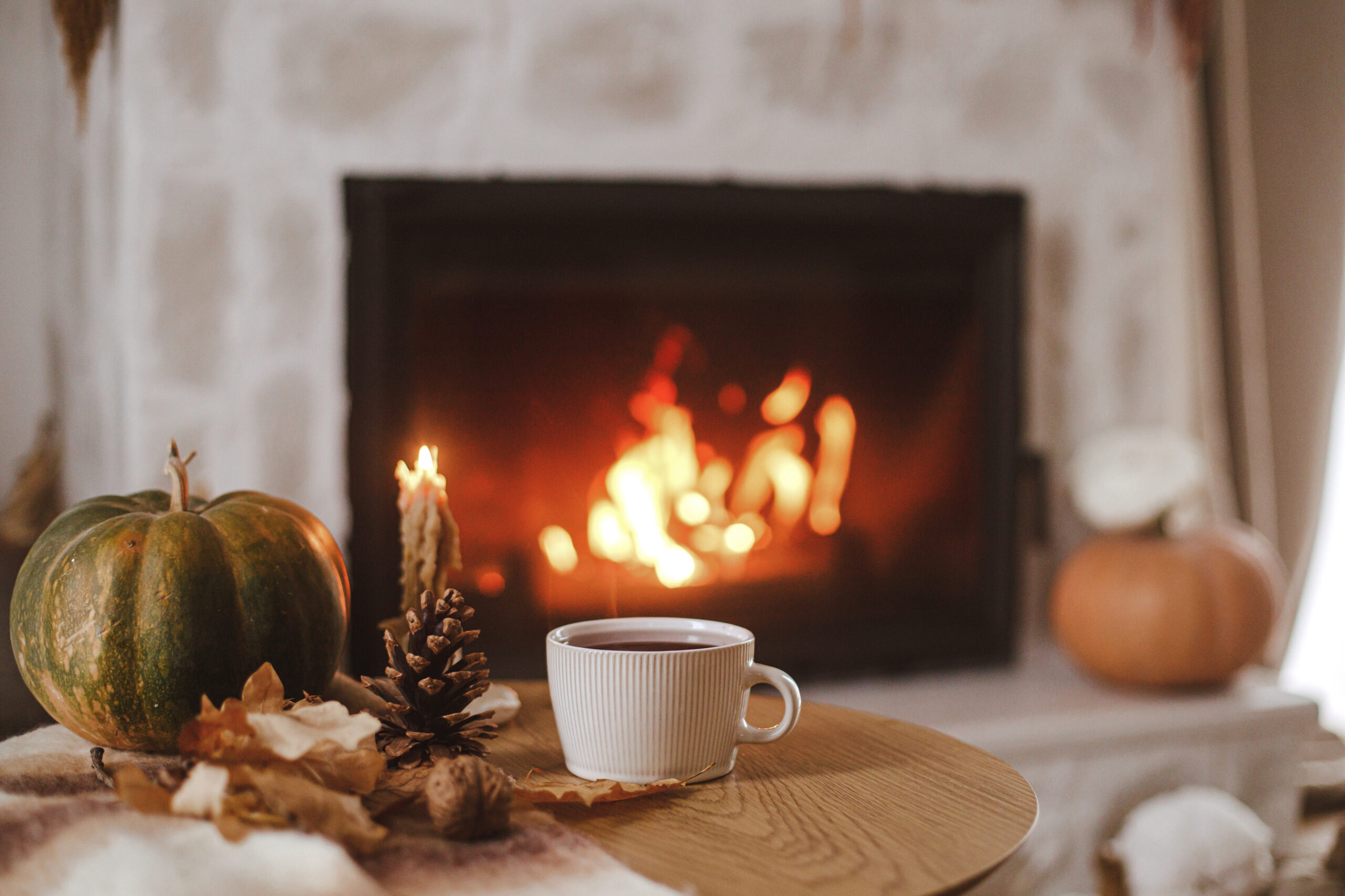 Warm cup of tea, pumpkin, autumn leaves on wooden table on background of burning fireplace. Cozy autumn still life. Thanksgiving and Halloween. Fall hygge